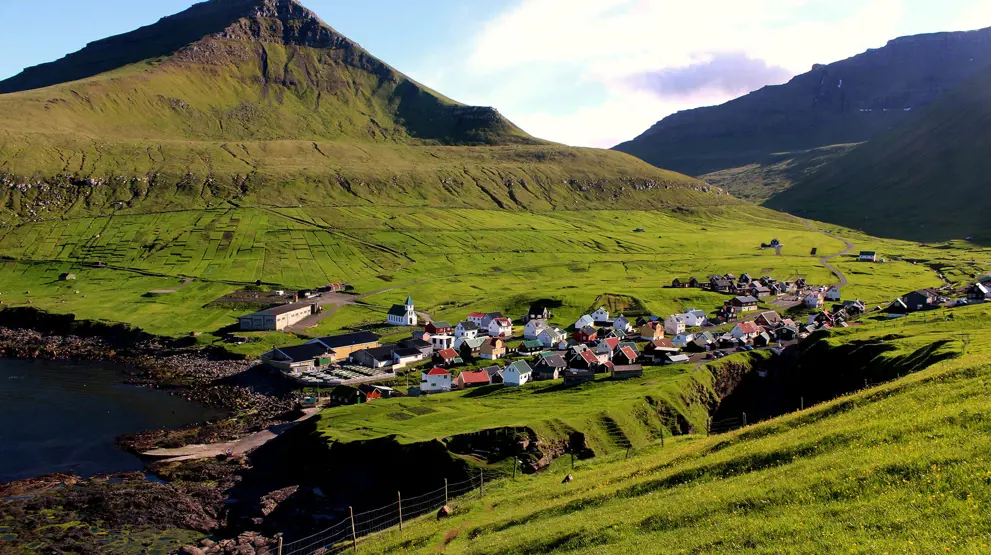 Gjogv ligger idyllisk til mellom de grønne fjellene - besøk den på reisen til Færøyene